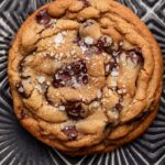 Close-up of a baked chocolate filled cookie topped with sea salt on a textured baking tray