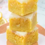 Lemon Brownies – The Best Zesty Dessert You’ll Ever Make 2 Stacked lemon brownies with glaze on a peach plate